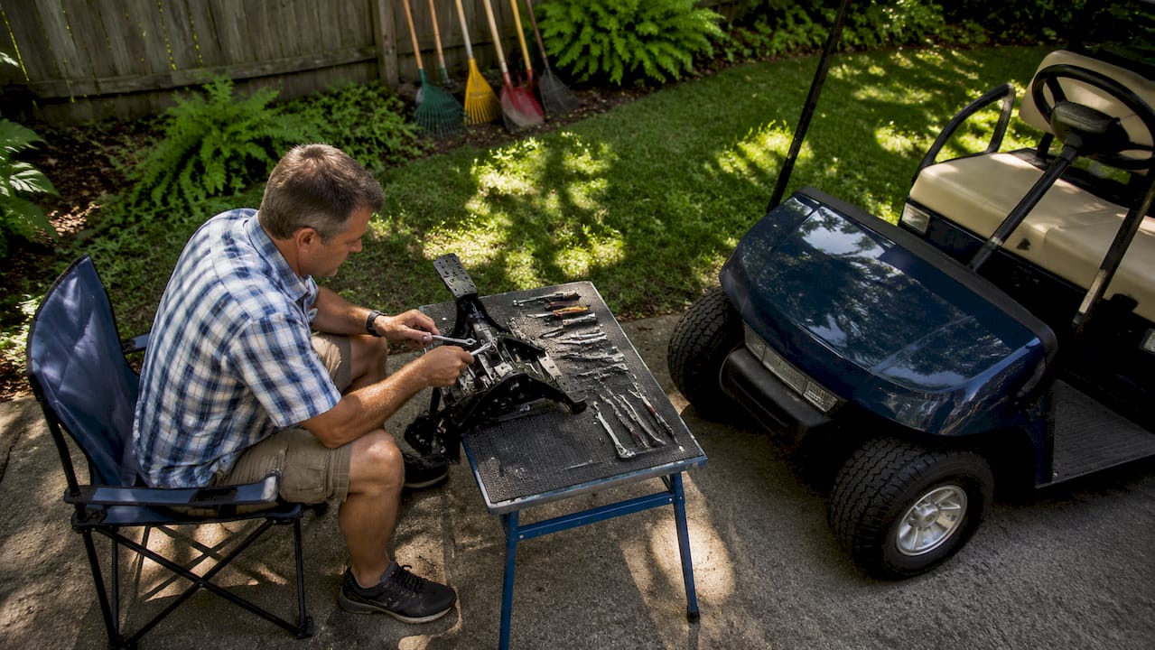Man adjusting golf cart pedal assembly in workshop